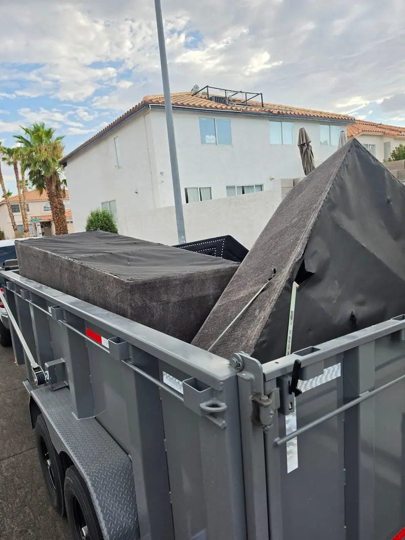 Spa cover and panels loaded high in the Legend Hauling trailer beside a two-story stucco home